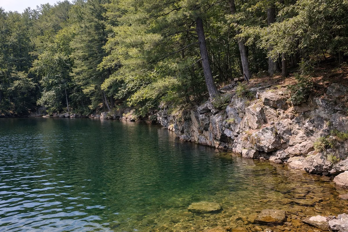 Clear deep green lake water against a steep rocky bank with overhanging trees